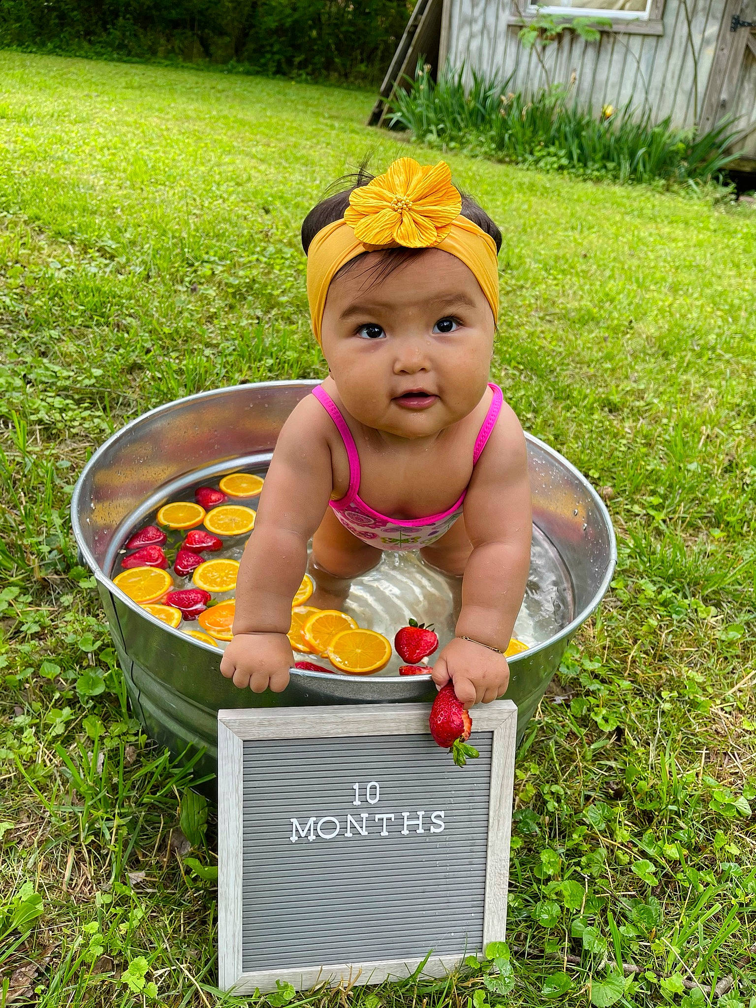 Kali is registered to the contest to win money with this photo: baby, baby_products, child, face, fruit, fun, garden, grass, happy, hat, head, headwear, leisure, natural_foods, people_in_nature, person, plant, play, recreation, sitting