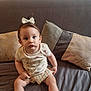 baby, bow, child, clothing, couch, cute, expression, face, furniture, home, indoor, looking, pattern, person, pillow, portrait, sitting, textile, toddler, young
