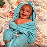 Noah is registered to the contest to win money with this photo: baby, child, smiling, blue_towel, hooded_towel, quilt, blanket, happy, indoors, infant, cute, person, portrait, laying, soft_texture, wrapped, skin, face, young, cozy