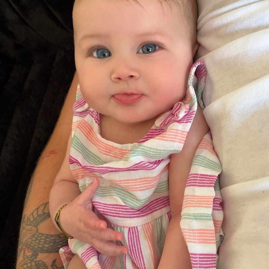 Navayla is registered to the contest to win money with this photo: arm, baby, baby_clothes, blue_eyes, child, closeup, cute, fingers, hand, happy, human, indoor, infant, person, portrait, sitting, skin, smiling, striped_dress, tattoo