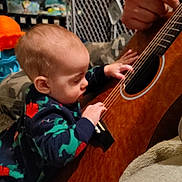 Stanley Cash joined the competition — help win amazing prizes! baby, child, guitar, music, hand, onesie, dinosaur_pattern, indoor, carpet, toy, adult, string_instrument, furniture, floor, curious, playing, interaction, person, closeup, home