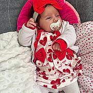élya participe au concours pour gagner de l'argent avec cette photo : baby, infant, pacifier, red_bow, heart_pattern, white_clothing, blanket, bedding, soft_texture, cute, child, indoors, resting, headband, sock, lying_down, comfort, portrait, newborn, toddler