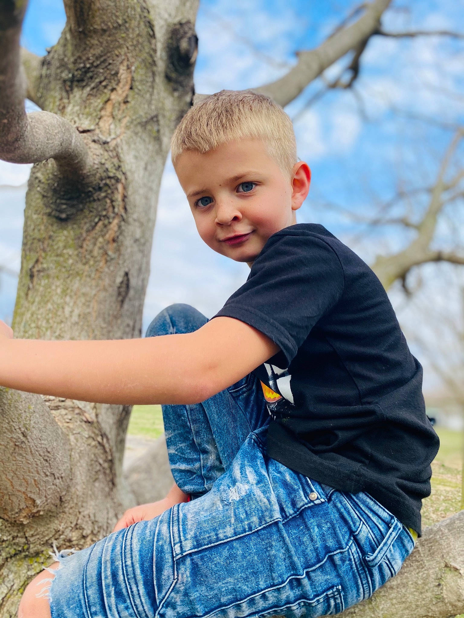 Colton is registered to the contest to win money with this photo: arm, azure, blue, botany, eye, gesture, grass, happy, joint, leaf, leisure, people_in_nature, person, plant, shoulder, sky, toddler, tree, trunk, wood