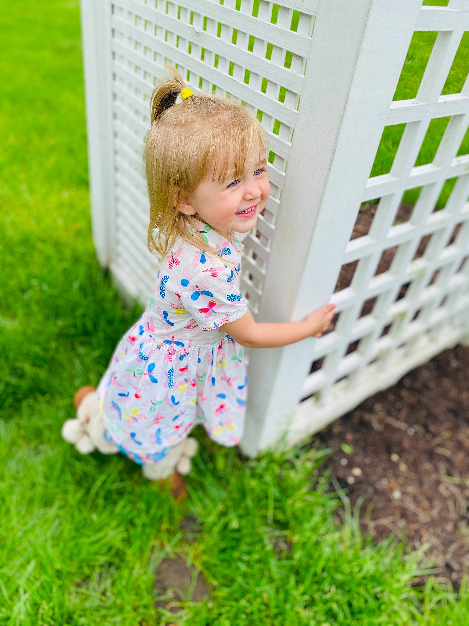 Alanna is registered to the contest to win money with this photo: baby, baby_toddler_clothing, barefoot, child, clothing, dress, fence, fun, garden, grass, happy, leisure, mammal, mesh, pattern, people_in_nature, person, plant, play, smile