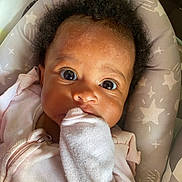 Harlem is registered to the contest to win money with this photo: baby, infant, child, face, eyes, clothing, pink, mitten, hand, cushion, pattern, stars, seat, portrait, closeup, expression, soft_lighting, indoor, cute, young