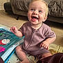 baby, child, smiling, happy, indoor, sitting, playmat, toy, blue_eyes, blond_hair, onesie, carpet, couch, pillow, home, person, infant, cute, cheerful, portrait