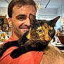 Daisy Mae joined the competition — help win amazing prizes! man, cat, tortoiseshell_cat, indoor, smile, portrait, pet, animal, fur, yellow_eyes, face, human, holding, arm, casual_clothing, hair, whiskers, expression, background_blur, store
