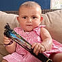 baby, blue_wall, child, couch, curious, face, fan, foot, furniture, hand, holding_object, home, indoor, person, pink_dress, portrait, sitting, skin, striped_clothing, window