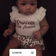 Kamyia is registered to the contest to win money with this photo: baby, infant, child, sitting, clothing, white_shirt, leopard_print, text_overlay, countdown_timer, portrait, cute, face, legs, dark_background, soft_focus, young_child, person, expression, casual, indoors