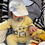 Laïon participe au concours pour gagner de l'argent avec cette photo : baby, pacifier, yellow_outfit, cap, plush_toy, stroller, zebra_pattern, child, hand, soft_toy, sunlight, comfort, cute, infant, sitting, outdoor, clothing, headwear, playful, relaxed