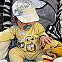 baby, pacifier, yellow_outfit, cap, plush_toy, stroller, zebra_pattern, child, hand, soft_toy, sunlight, comfort, cute, infant, sitting, outdoor, clothing, headwear, playful, relaxed