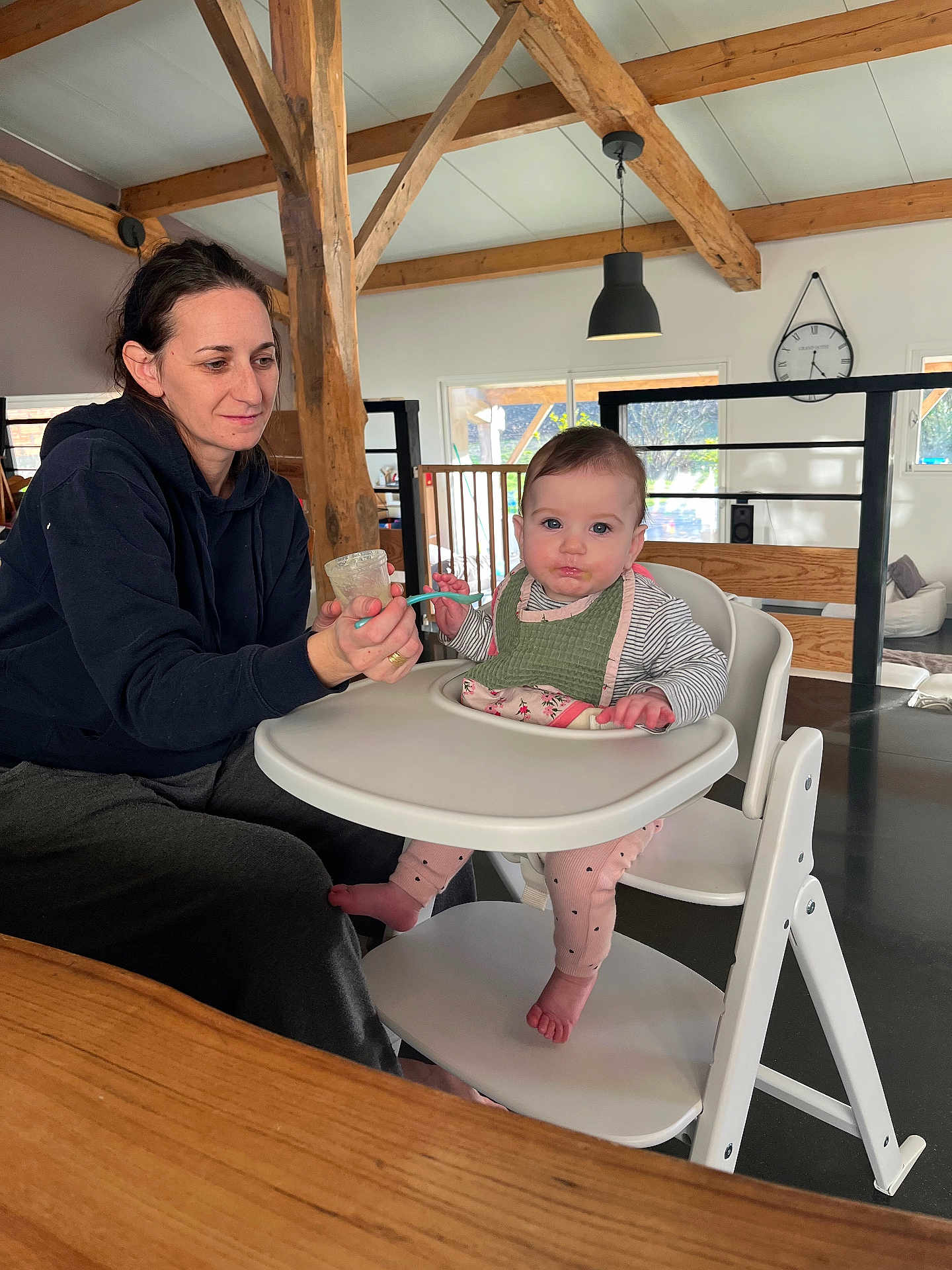 Rose a rejoint le concours — aidez-le/la à gagner de superbes lots ! baby, woman, feeding, high_chair, bib, spoon, indoor, wooden_beams, clock, window, table, floor, furniture, person, child, casual_clothing, light, home, parenting, care