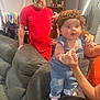 Ellie Bea joined the competition — help win amazing prizes! baby, denim_overalls, yarn_wig, couch, man, neon_cap, red_shirt, living_room, furniture, person, indoor, hand_holding, pink_socks, cabinet, refrigerator, curious_expression, casual_clothing, home, adult, child