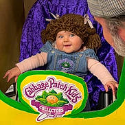 Ellie Bea is registered to the contest to win money with this photo: adult, baby, beard, cabbage_patch_kids, child, clothing, collectors_club, cutout, denim_overalls, face, happy, hat, indoor, person, playful, portrait, purple_background, seated, smiling, yarn_wig