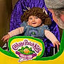adult, baby, beard, cabbage_patch_kids, child, clothing, collectors_club, cutout, denim_overalls, face, happy, hat, indoor, person, playful, portrait, purple_background, seated, smiling, yarn_wig