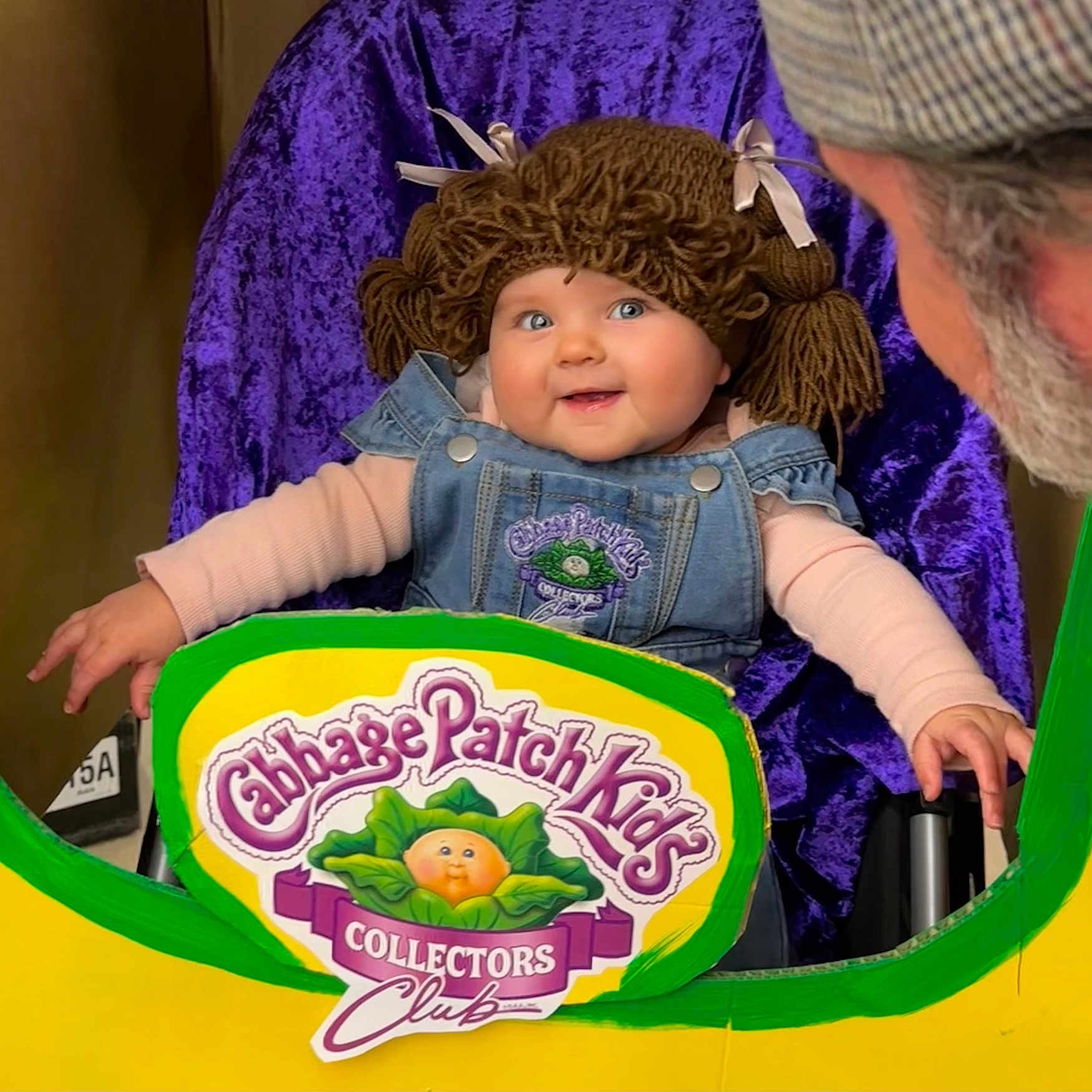 Ellie Bea is registered to the contest to win money with this photo: adult, baby, beard, cabbage_patch_kids, child, clothing, collectors_club, cutout, denim_overalls, face, happy, hat, indoor, person, playful, portrait, purple_background, seated, smiling, yarn_wig