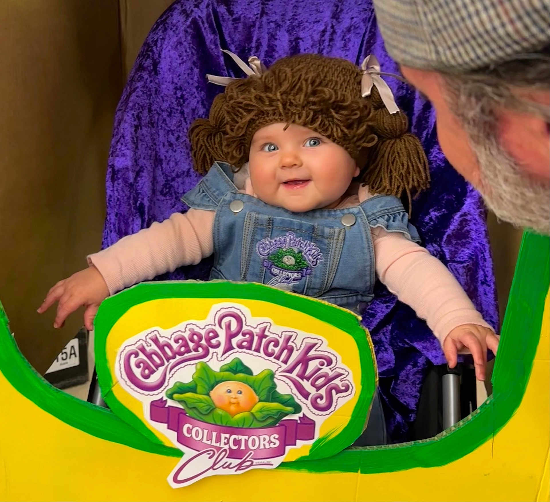 Ellie Bea is registered to the contest to win money with this photo: adult, baby, beard, cabbage_patch_kids, child, clothing, collectors_club, cutout, denim_overalls, face, happy, hat, indoor, person, playful, portrait, purple_background, seated, smiling, yarn_wig
