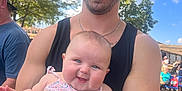 Ellie Bea is registered to the contest to win money with this photo: man, baby, smile, outdoor, sunglasses, tank_top, tattoo, arm, child, holding, happy, people, trees, daylight, casual_clothing, denim, floral, background, scooter, sunny