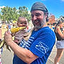 baby, man, corn, food, outdoor, festival, crowd, smiling, beard, blue_shirt, hat, woman, sunny, trees, stroller, people, daytime, clothing, holding, fun
