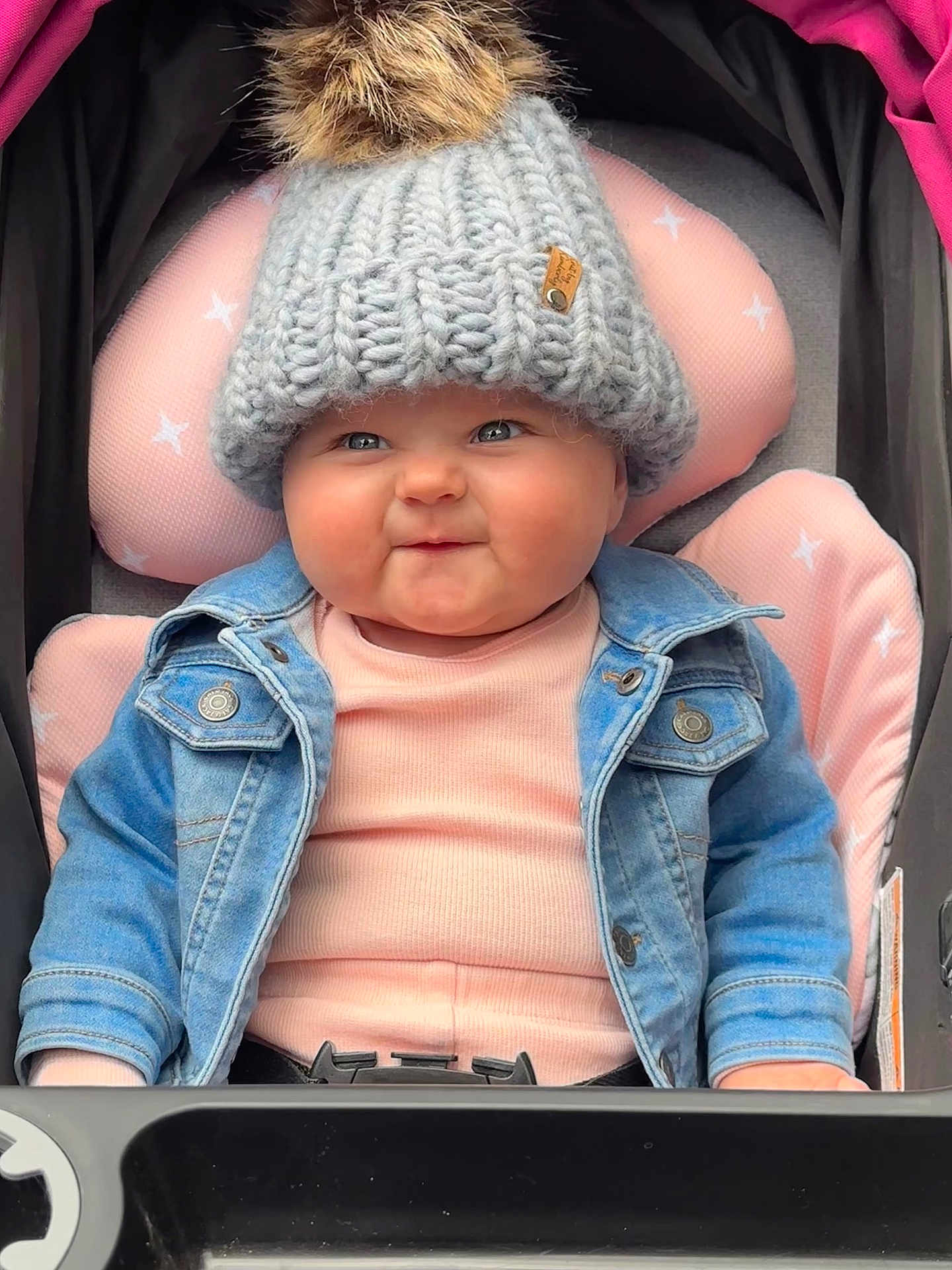 Ellie Bea is registered to the contest to win money with this photo: baby, child, face, hat, knit_hat, pom_pom, denim_jacket, pink, stroller, cushion, smile, cheeks, clothing, cute, infant, seated, portrait, warm_clothing, cozy, outdoor