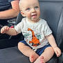 baby, child, dinosaur_shirt, blue_eyes, car_seat, smiling, barefoot, shorts, infant, cute, happy, sitting, person, casual_clothing, indoor, light_skin, short_hair, cute_expression, human, family