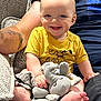 Ryder is registered to the contest to win money with this photo: baby, child, smiling, yellow_shirt, plush_toy, elephant_toy, couch, arm, tattoo, barefoot, indoor, happy, person, seated, soft_toy, fabric, texture, closeup, cute, comfort