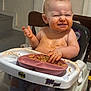 baby, child, high_chair, spaghetti, messy, food, meal_time, plate, happy, face, expression, indoor, pants, clothing, hand, sitting, batman_sticker, tongue, cute, funny