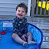toddler, child, pool, water, outdoor, smile, curly_hair, blue_eyes, play, deck, sunlight, clothing, toy, happy, sitting, skin, feet, person, summer, blue