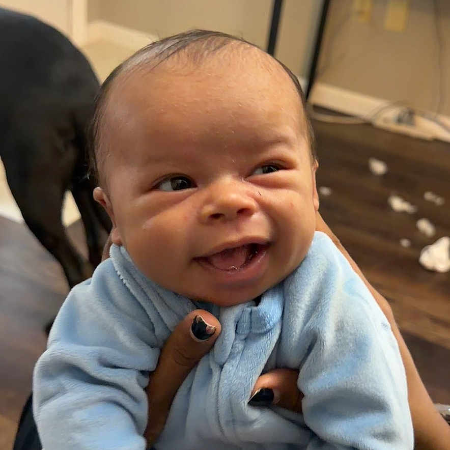 Torrin joined the competition — help win amazing prizes! baby, blue_onesie, closeup, couch, cute, dog_back, door, expression, fingernails, floor_debris, hands, happy, indoor, infant, living_room, person_holding, portrait, smile, television, wood_floor