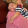 Ilanna joined the competition — help win amazing prizes! baby, child, person, indoor, couch, red_and_white_checkered_shirt, striped_shirt, sleeping, holding, portrait, face, hand, furniture, wood_paneling, painting, picture_frame, skin, hair, closeup, comfort