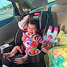 Cataleya is registered to the contest to win money with this photo: toddler, child, car_seat, car_interior, snack, doll, toy, sunlight, seatbelt, smile, happy, baby_food, plastic_bag, window, road, traffic_light, clothing, foot, seat, recline