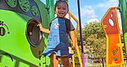 Nayana is registered to the contest to win money with this photo: child, toddler, playground, outdoor, smiling, denim_overalls, blue_sky, play_equipment, colorful, green, orange, yellow, purple, trees, sunlight, happy, person, feet, socks, daytime