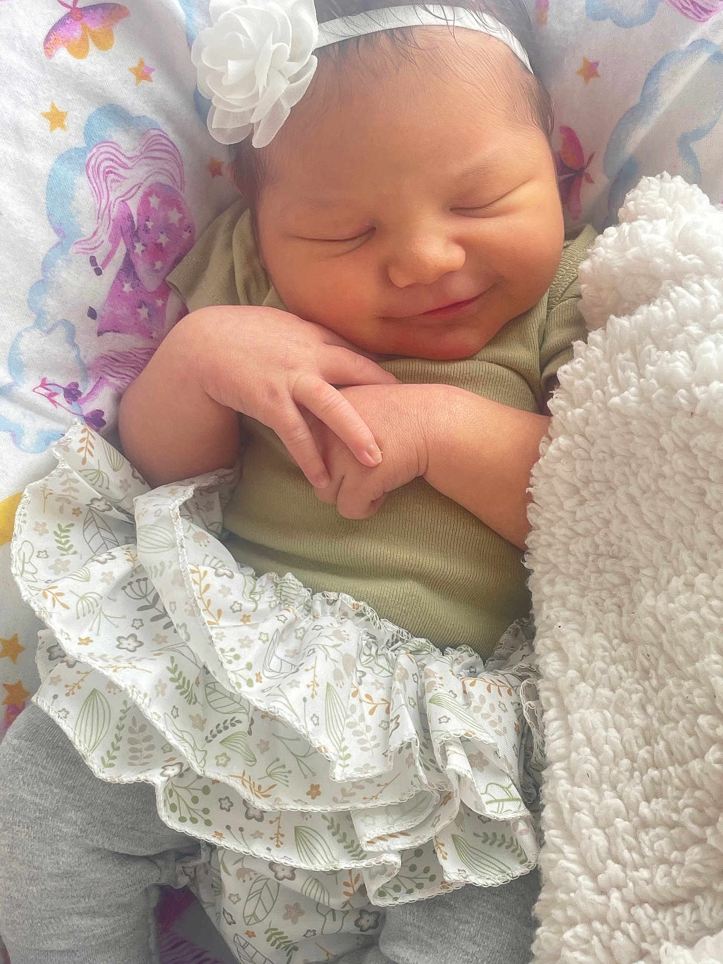 Alannah joined the competition — help win amazing prizes! baby, newborn, smiling, headband, flower, blanket, patterned_sheet, unicorn, stars, hands, clothing, ruffle_skirt, gray_pants, sleeping, soft_texture, cute, infant, closeup, peaceful, indoor
