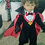 child, costume, vampire, cape, indoor, carpet, laundry, clothes, person, portrait, cute, toddler, black_clothing, red_clothing, fun, holiday, party, dress_up, young_child, curly_hair