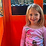 child, girl, smile, face, long_hair, pink_shirt, princess_characters, patterned_pants, orange_background, reflection, window, seated, happy, portrait, indoor, person, clothing, casual, cute, bright_colors