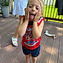 Paisley joined the competition — help win amazing prizes! child, girl, barefoot, red_shirt, navy_shorts, deck, outdoor, playful, tongue_out, hands_on_cheeks, person, summer, sunlight, greenery, wooden_floor, adult, casual_clothing, funny_face, fence, toy