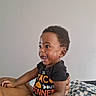 Damarion Gooden is registered to the contest to win money with this photo: toddler, child, baby, smiling, happy, sitting, portrait, indoor, bed, blanket, adult_arm, support, black_shirt, curly_hair, open_mouth, looking_away, home, cozy, photography, person