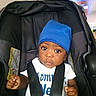 Damarion Gooden is registered to the contest to win money with this photo: baby, black_fabric, blue_hat, car_seat, child, closeup, eyes, face, hands, home, indoors, infant, photography, portrait, safety_harness, serious_expression, sitting, stroller, television, white_shirt