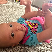 Meyli joined the competition — help win amazing prizes! baby, infant, onesie, superhero_logo, pink_tutu, bed, blanket, patterned_sheet, feet, hands, big_eyes, portrait, close_up, lying_down, skin, cute, indoor, furniture, television, parent_hand