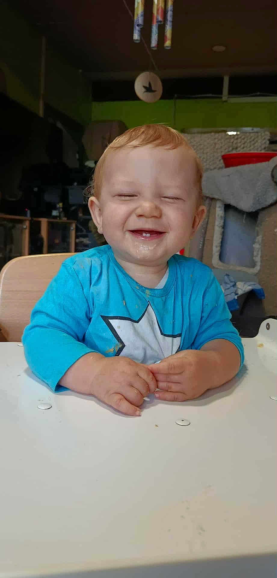 Emrys participe au concours pour gagner de l'argent avec cette photo : toddler, child, smiling, happy, messy, blue_shirt, star, indoor, table, hands, face, hair, teeth, furniture, background, cozy, seat, expression, person, young_child