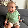 Tobias a rejoint le concours — aidez-le/la à gagner de superbes lots ! baby, child, smiling, sitting, green_shirt, shorts, couch, blanket, toys, indoors, face, happy, person, skin, foot, hand, head, casual_clothing, living_room, cute