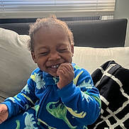 Cairo joined the competition — help win amazing prizes! toddler, child, smiling, laughing, blue_onesie, dinosaur_pattern, cozy, indoor, couch, blanket, window_blinds, natural_light, happy, cute, person, home, furniture, childhood, portrait, seated