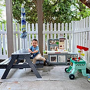 Zain joined the competition — help win amazing prizes! toddler, child, play, toy, picnic_bench, outdoor, patio, fence, kitchen_set, smile, happy, greenery, umbrella, concrete_floor, plastic_toys, casual_clothing, daylight, person, fun, recreation