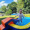 Zain is registered to the contest to win money with this photo: child, toddler, pool, inflatable, water, summer, outdoor, grass, tree, sunny, blue_sky, play, fun, smile, clothing, shorts, long_sleeve_shirt, backyard, nature, splash
