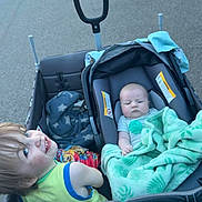 Greyson is registered to the contest to win money with this photo: baby, blanket, camouflage, car_seat, child, daytime, family, green_blanket, happy, holding, outdoor, pavement, person, sibling, sidewalk, smile, street, toddler, urban, wagon
