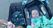 Greyson is registered to the contest to win money with this photo: baby, blanket, camouflage, car_seat, child, daytime, family, green_blanket, happy, holding, outdoor, pavement, person, sibling, sidewalk, smile, street, toddler, urban, wagon