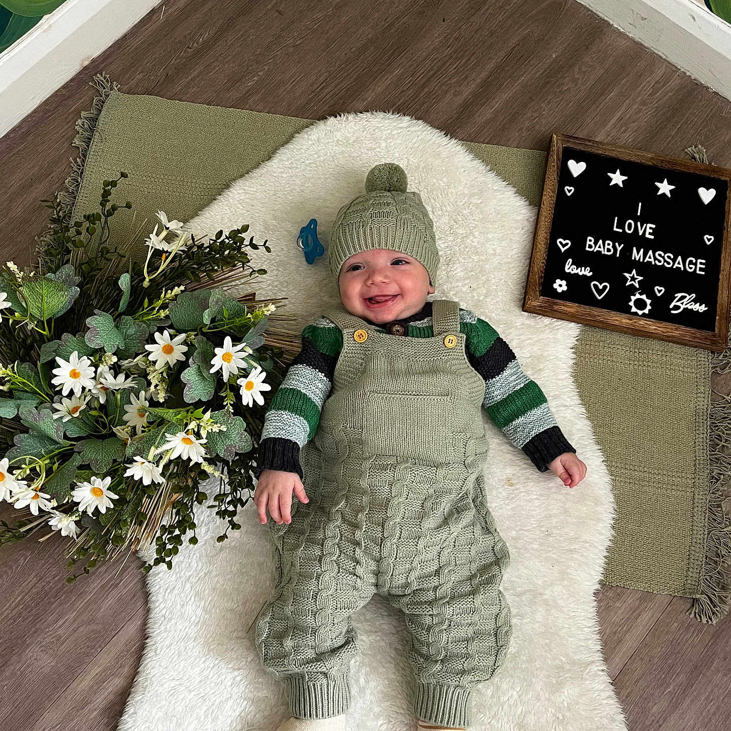 Reginald joined the competition — help win amazing prizes! baby, baby_accessory, child, cozy, cute, daisies, decor, flowers, green_clothing, happy, hat, indoor, knitted_clothing, laying_down, letter_board, plant, smiling, text_board, white_rug, wooden_floor