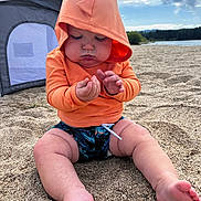 Maven is registered to the contest to win money with this photo: baby, child, hoodie, orange_clothing, beach, sand, tent, lake, water, sky, clouds, nature, outdoor, barefoot, cute, chubby, sitting, summer, playful, casual