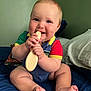 baby, child, infant, smiling, sitting, wooden_spoon, blue_bedspread, pillow, indoors, green_wall, cute, happy, cheeks, barefoot, clothing, short_sleeves, person, portrait, hand, toys