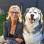 woman, dog, smiling, glasses, outdoor, grass, fence, happy, fluffy_dog, pet, nature, casual_clothing, sitting, portrait, daylight, person, animal, friendship, companionship, relaxation